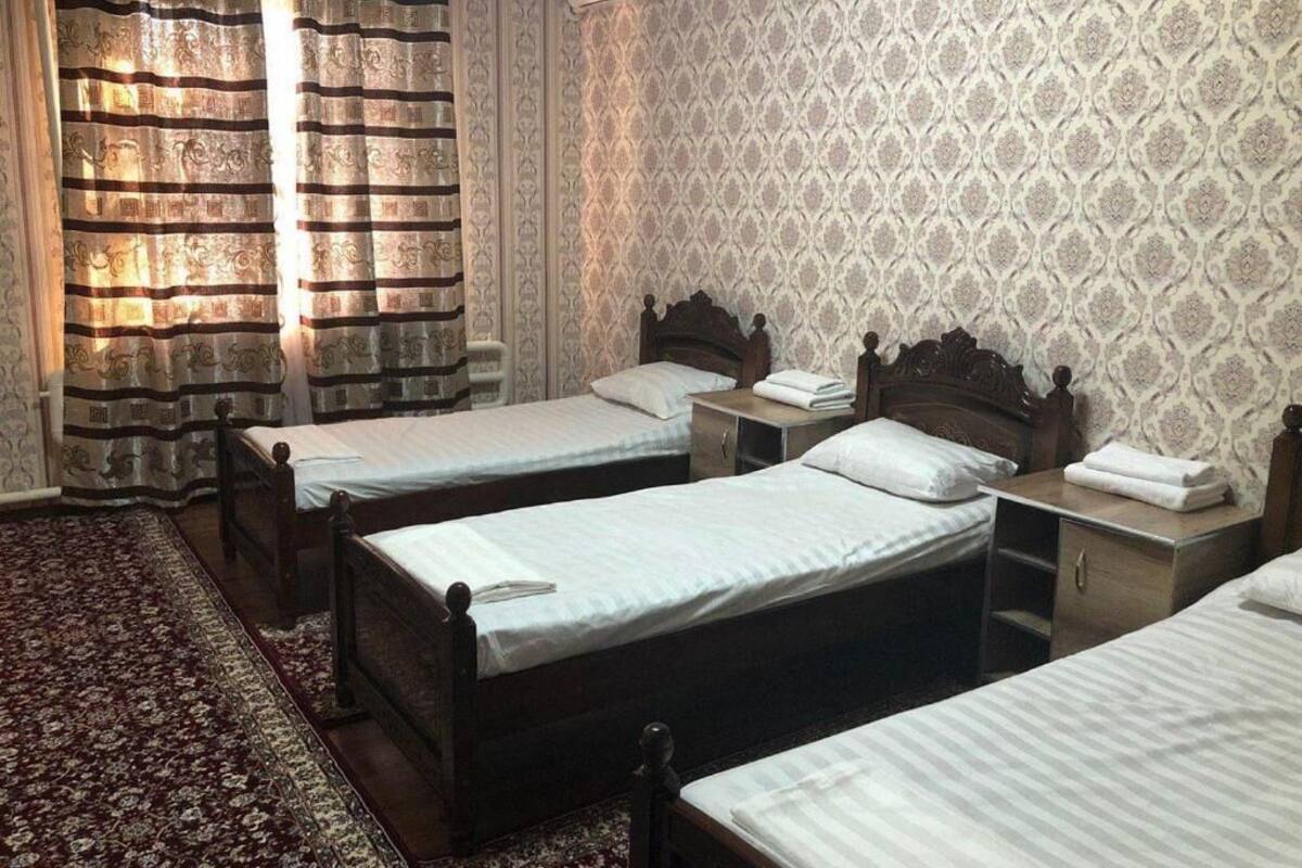 Ein Hotelzimmer mit drei Einzelbetten, einem gemusterten Wandteppich und einem dekorativen Vorhang.
