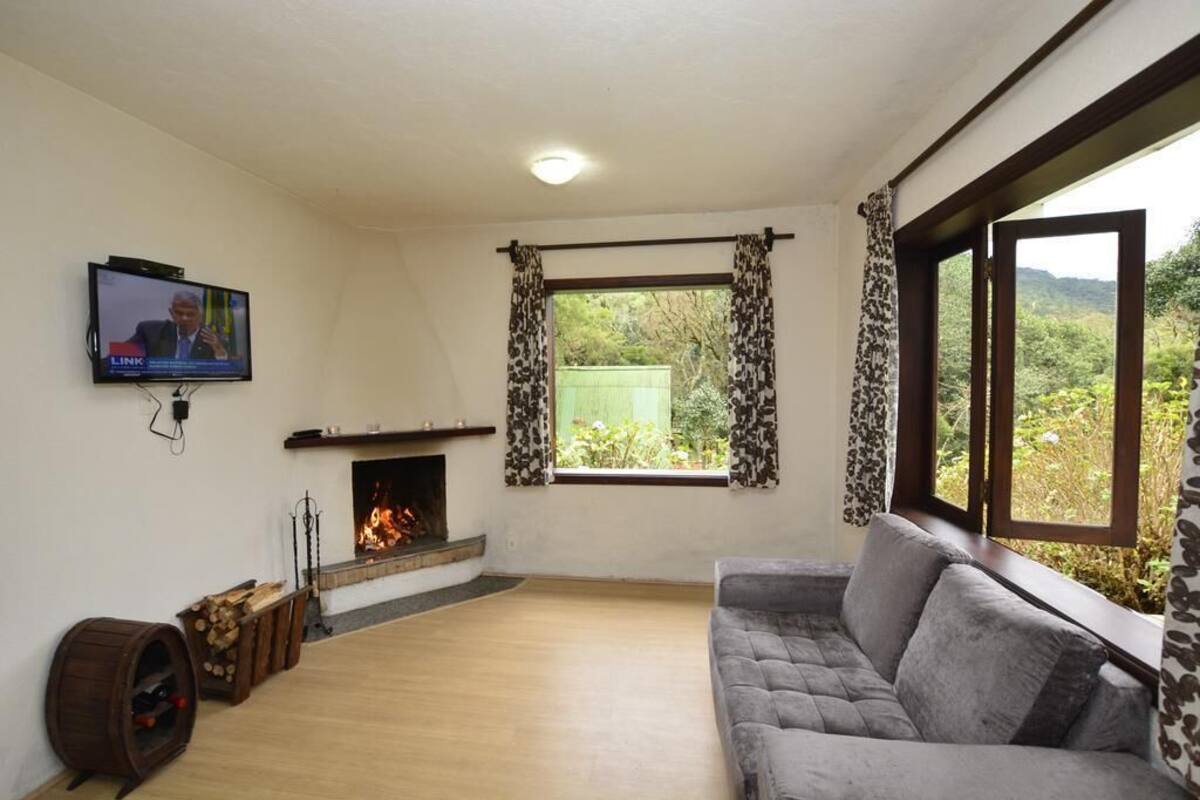 Ein Wohnzimmer mit Kamin, einer Couch, einem Fernseher und einem Fenster mit Vorhängen.