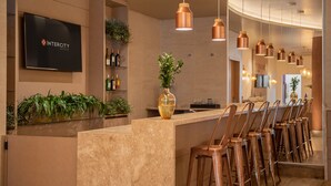 Un área de bar moderna con una barra larga, múltiples lámparas colgantes de cobre y un televisor mostrando 