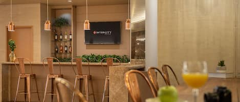 A modern hotel bar with copper chairs, a flat-screen TV, and a bar stocked with bottles.