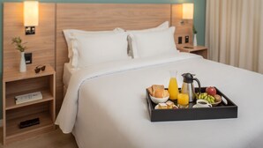 Una habitación de hotel con una cama bien hecha, una bandeja con alimentos para el desayuno y lámparas de noche.