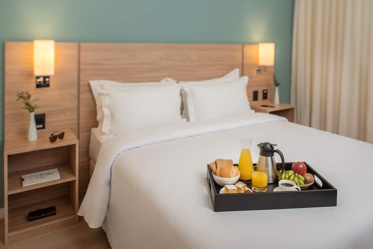 A hotel room with a neatly made bed, a tray of breakfast items, and bedside lamps.