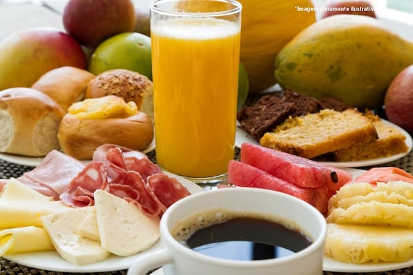Una mesa de desayuno con diversos alimentos, como pan, queso, embutidos, frutas y un vaso de zumo de naranja.
