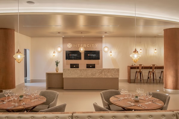 Un moderno vestíbulo de hotel con una recepción, zona de estar y espacio para comer.
