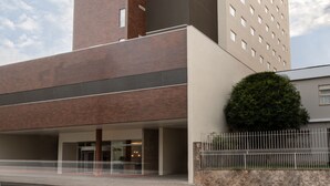 Un edificio moderno con fachadas de ladrillo y hormigón, que presenta una entrada amplia y un pequeño espacio verde.