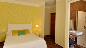 A hotel room with a bed, a bedside lamp, a wooden door, and a bathroom with a sink and shower. - Auberge de la Foret (Calenzana)
