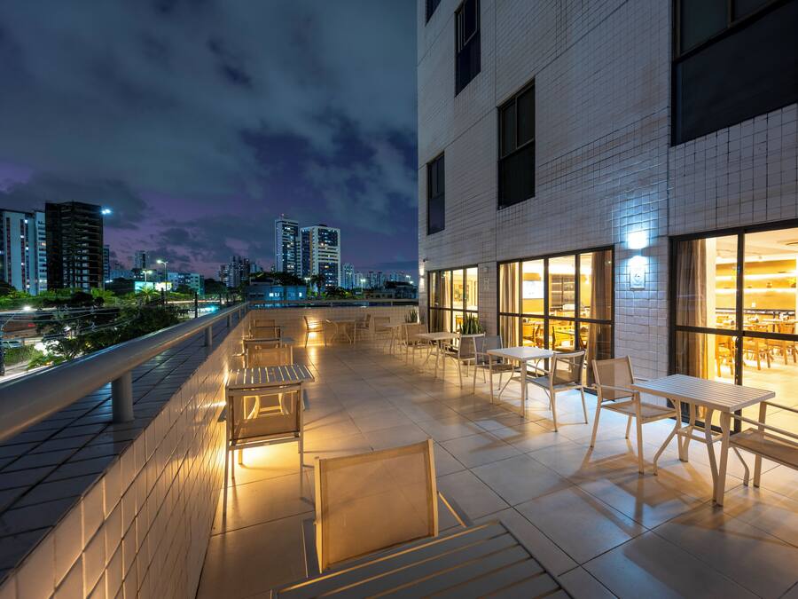An outdoor terrace with tables and chairs, a cityscape view, and a building with large windows.