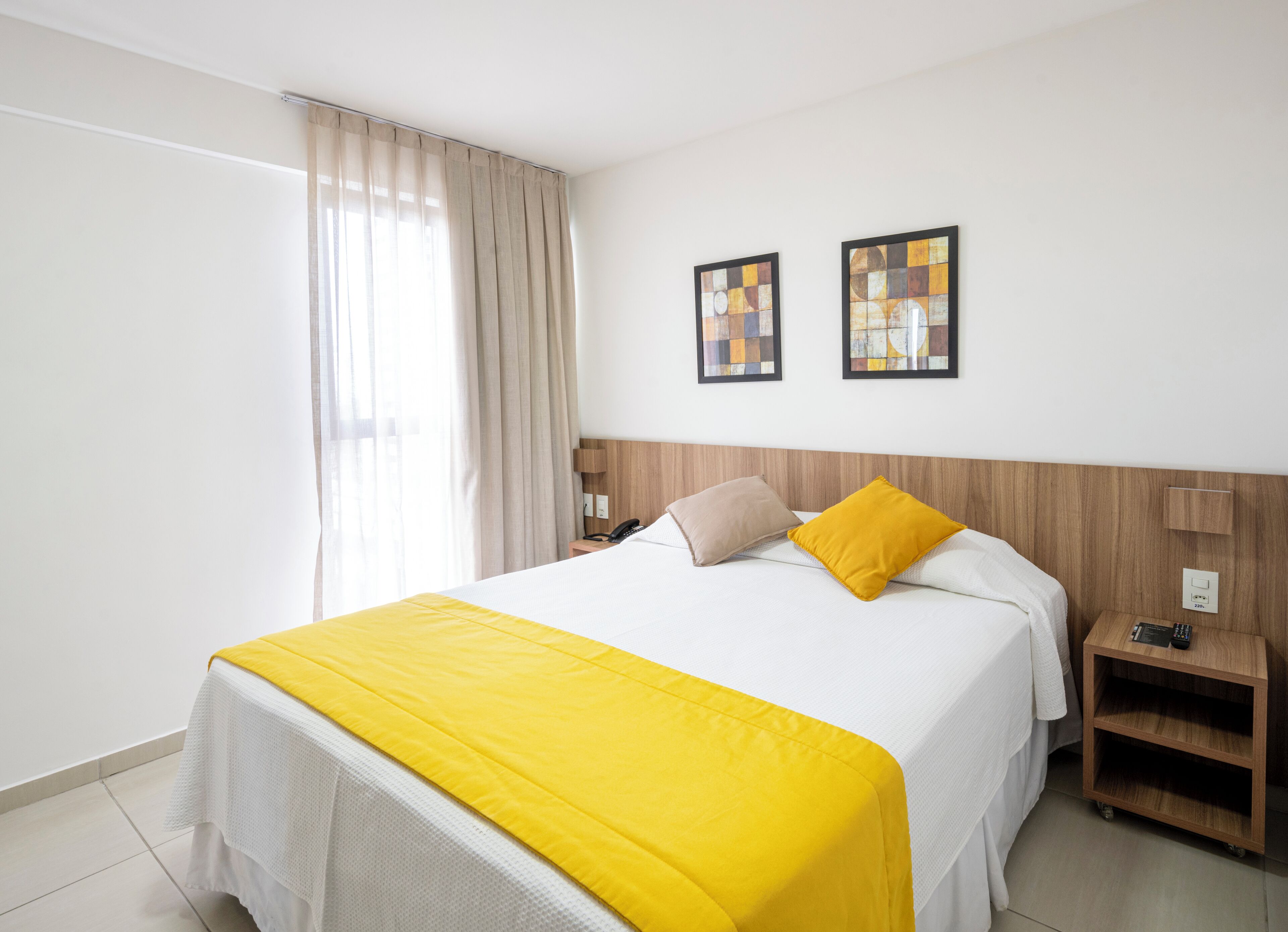 Una camera d'albergo con un letto, un comodino, una lampada e due quadri appesi al muro.