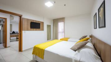 Quarto de hotel com duas camas, televisão de tela plana, cabeceira de madeira e banheiro visível por uma porta aberta.