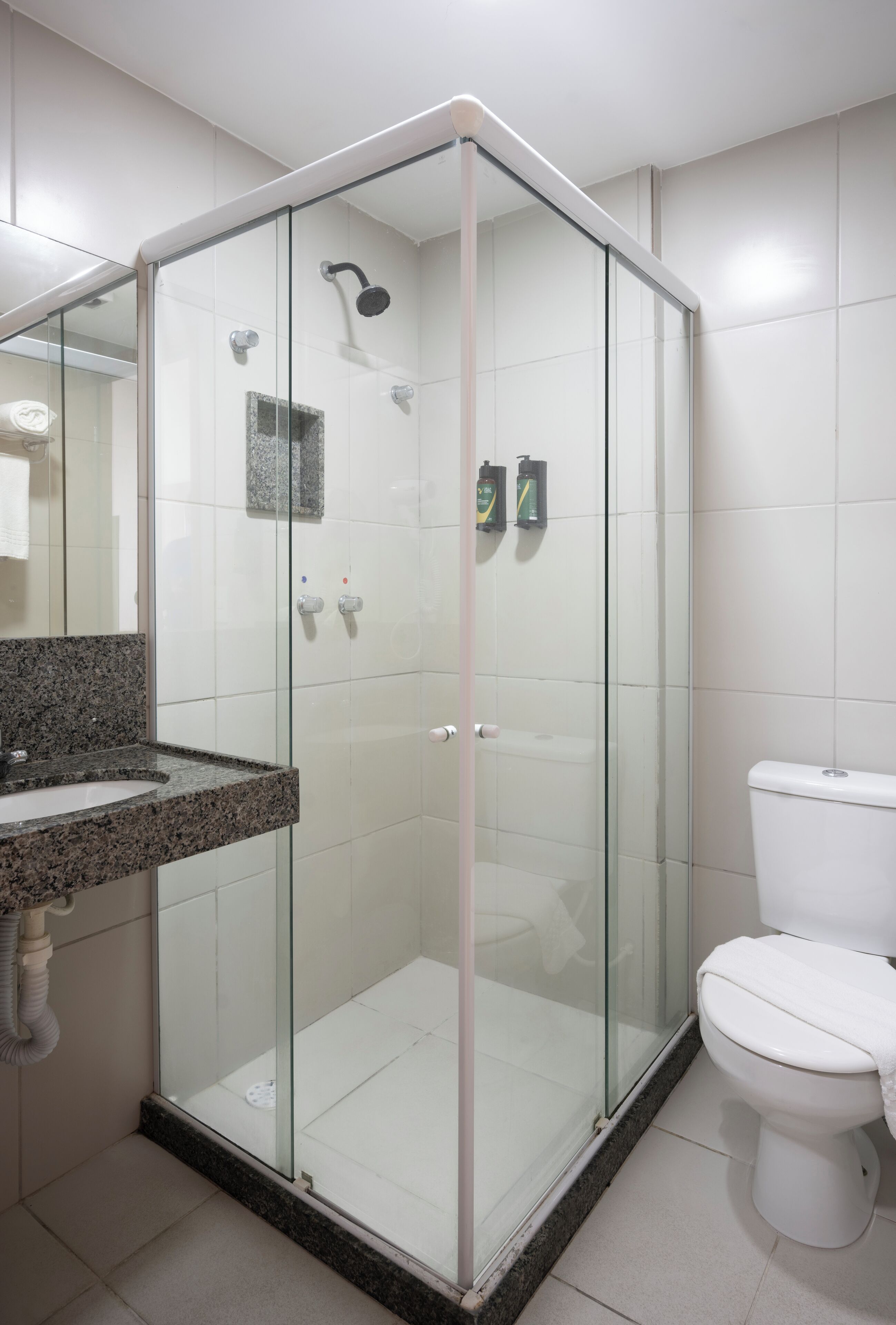 Un baño moderno con ducha de vidrio, inodoro blanco y lavamanos con encimera de granito.