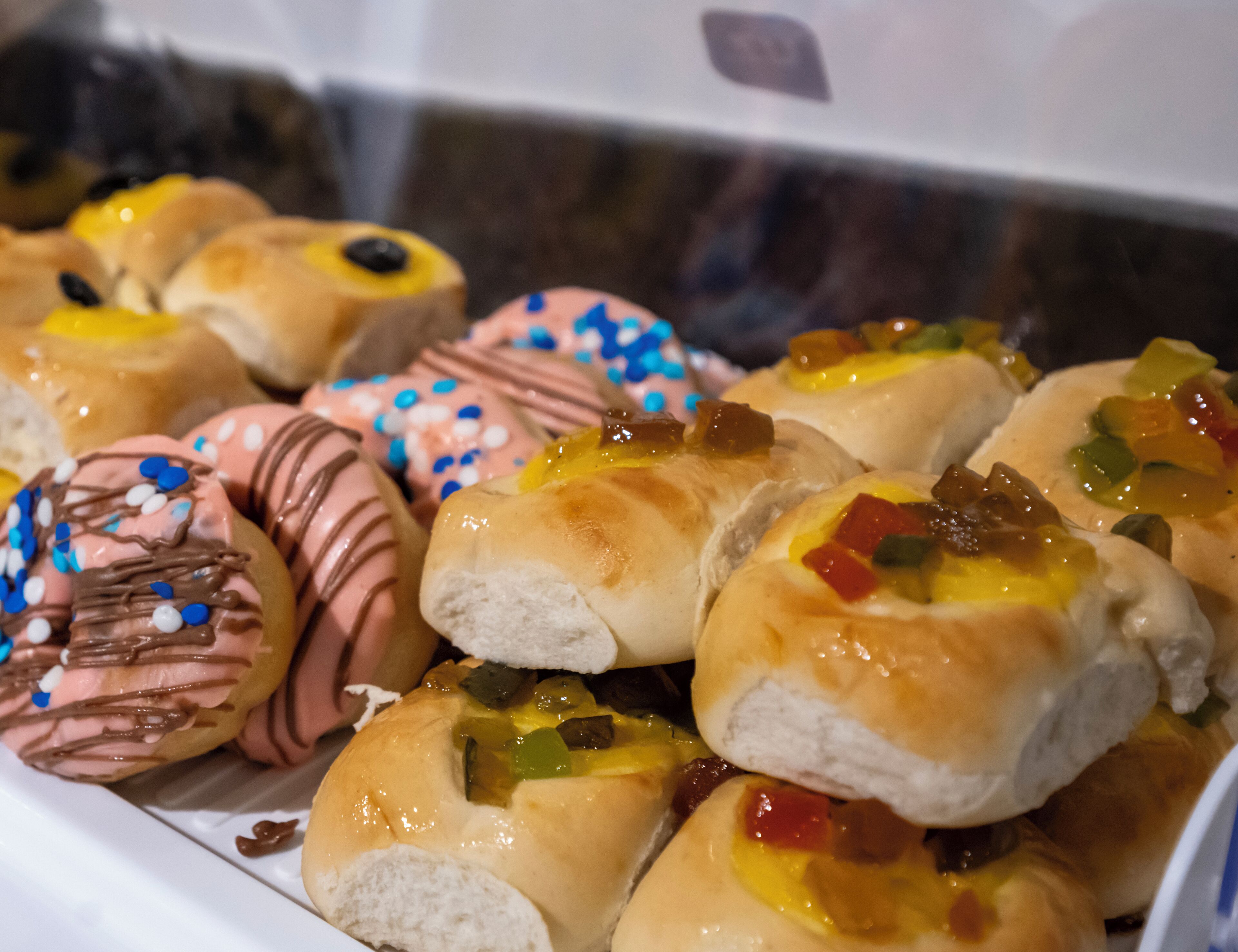 A display case with various pastries, including donuts and buns with toppings.