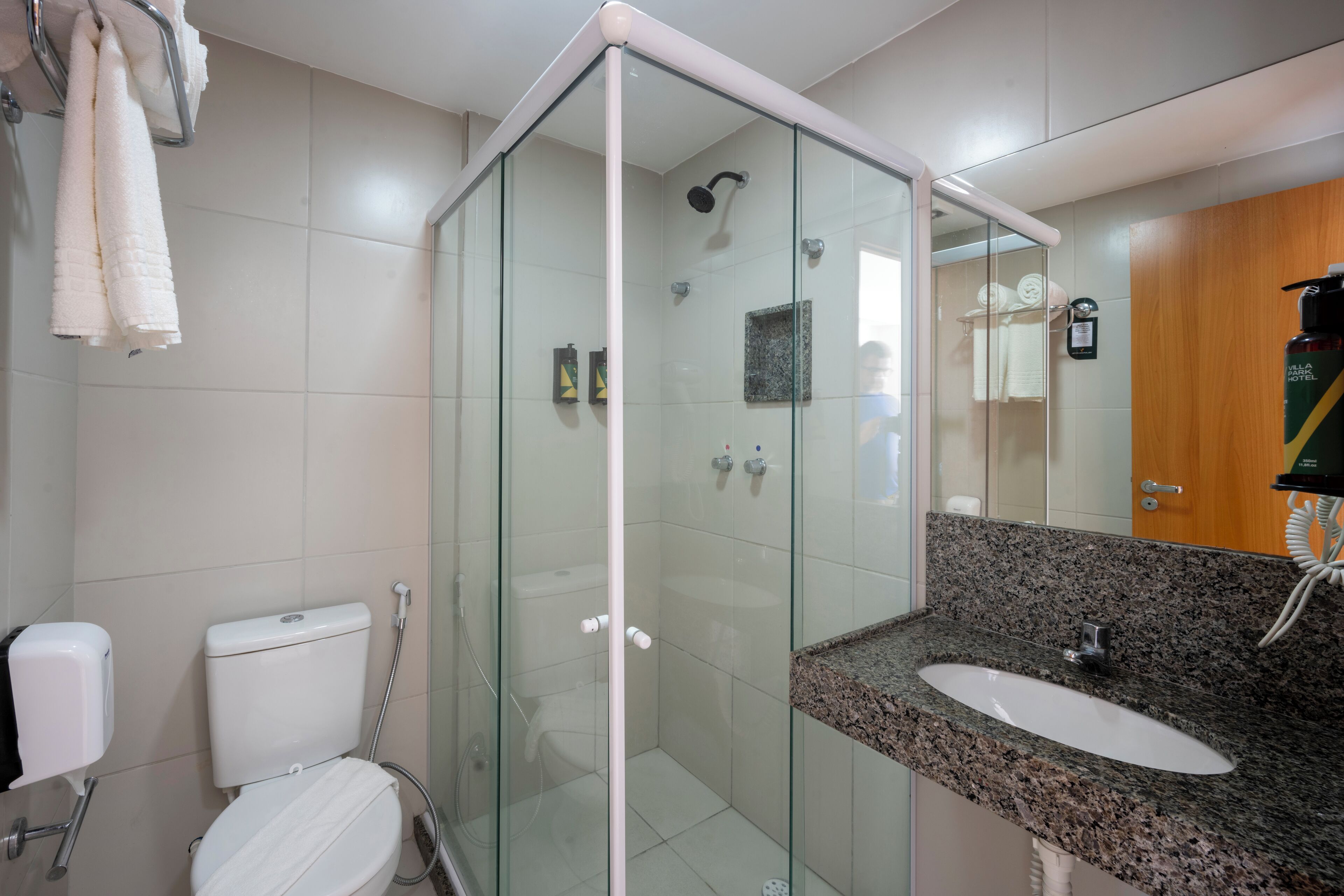 Un baño moderno con ducha envuelta en vidrio, inodoro blanco y lavamanos sobre encimera de granito.