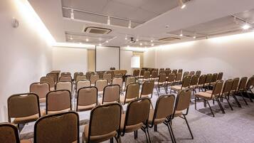 Un salón de conferencias con filas de sillas, una pantalla de proyector y una pizarra.
