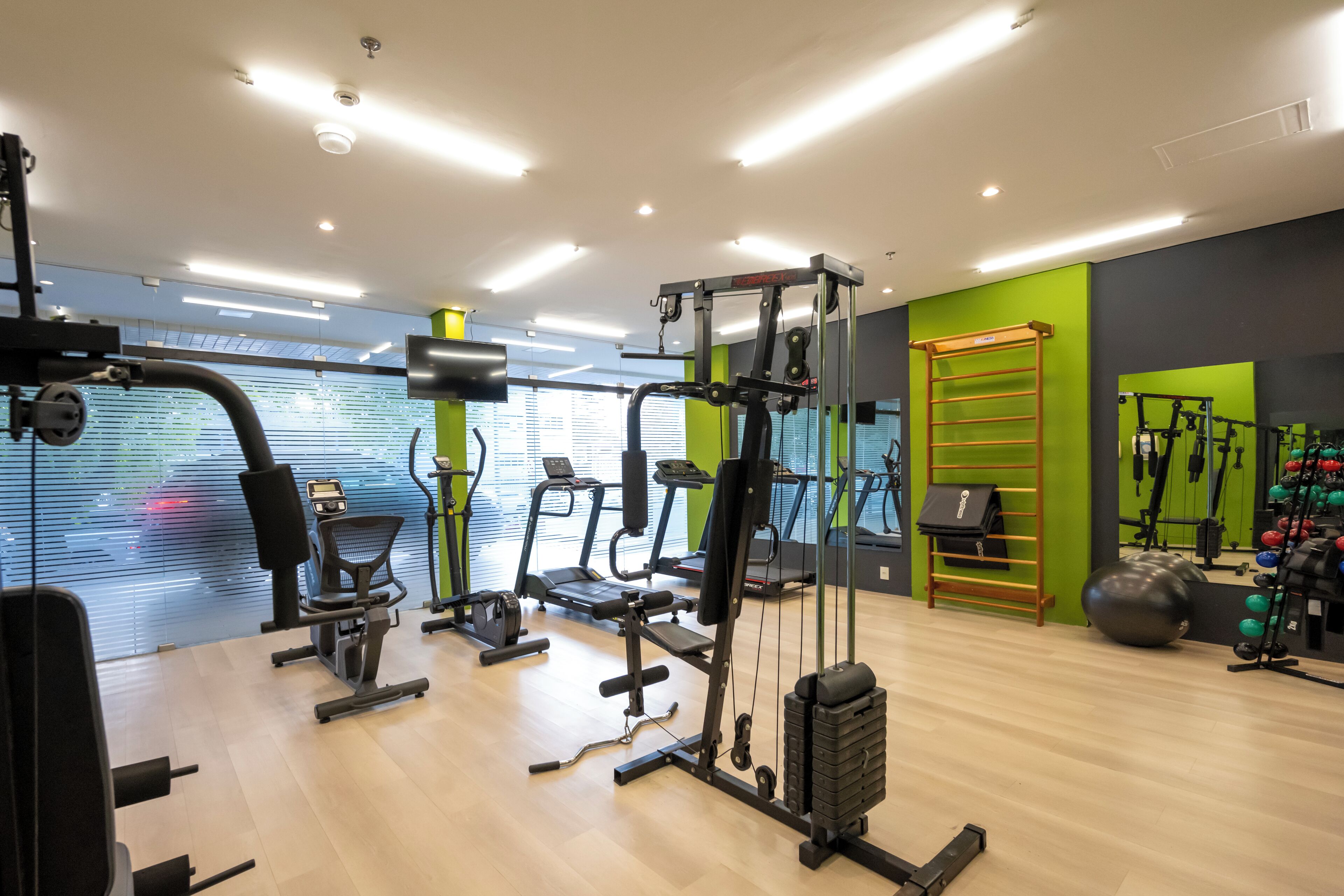 A gym with cardio machines, weightlifting equipment, and a green wall.