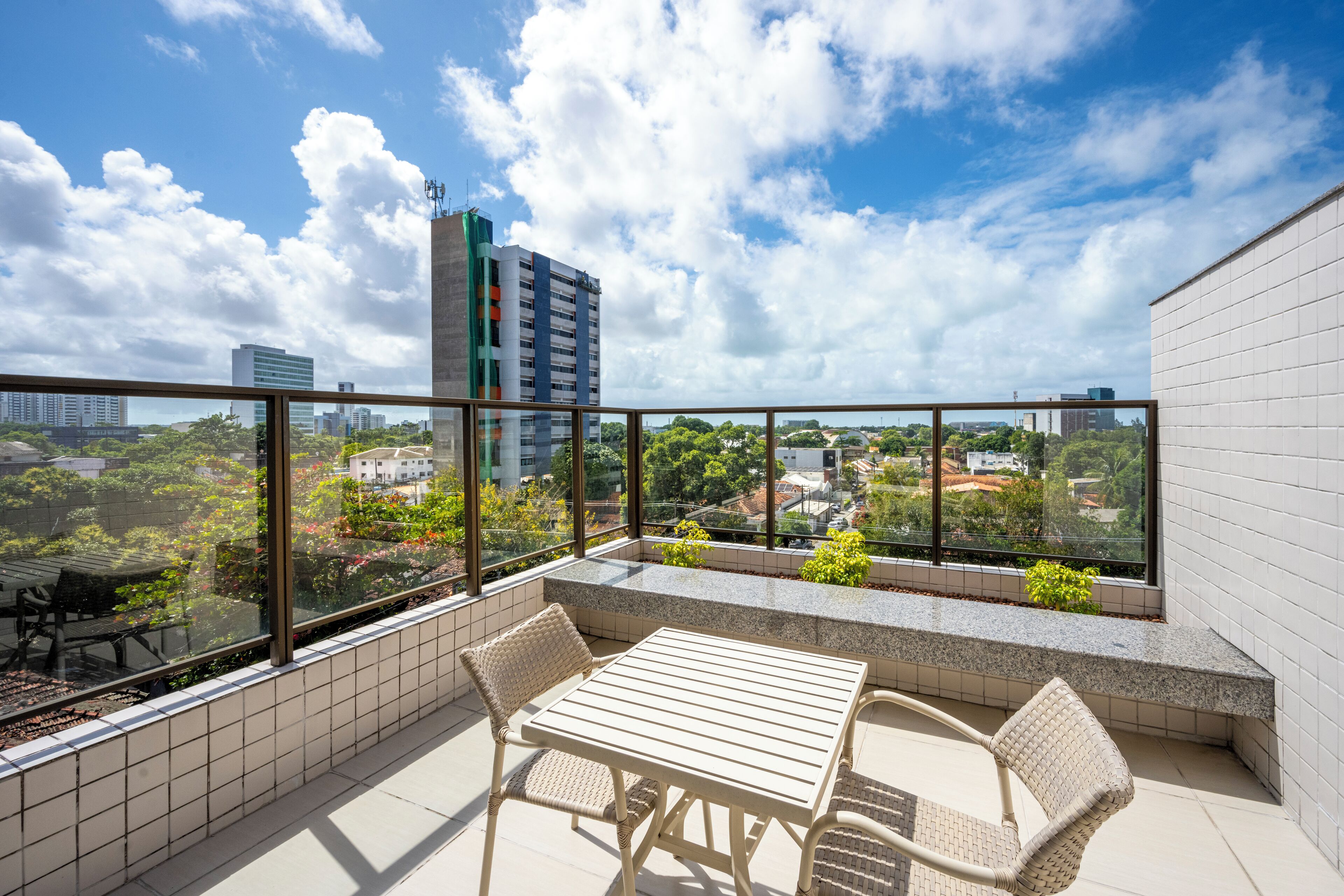 A balcony with a table and chairs, offering a view of a cityscape with buildings and greenery.