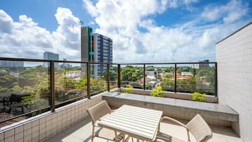 A balcony with a table and chairs, offering a view of a cityscape with buildings and greenery.