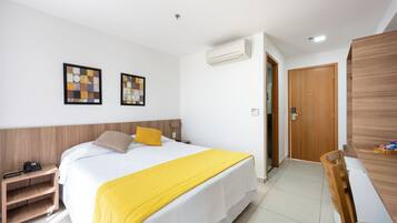 Una habitación de hotel moderna con una cama grande, una mesita de noche con teléfono, un escritorio con silla y un armario.