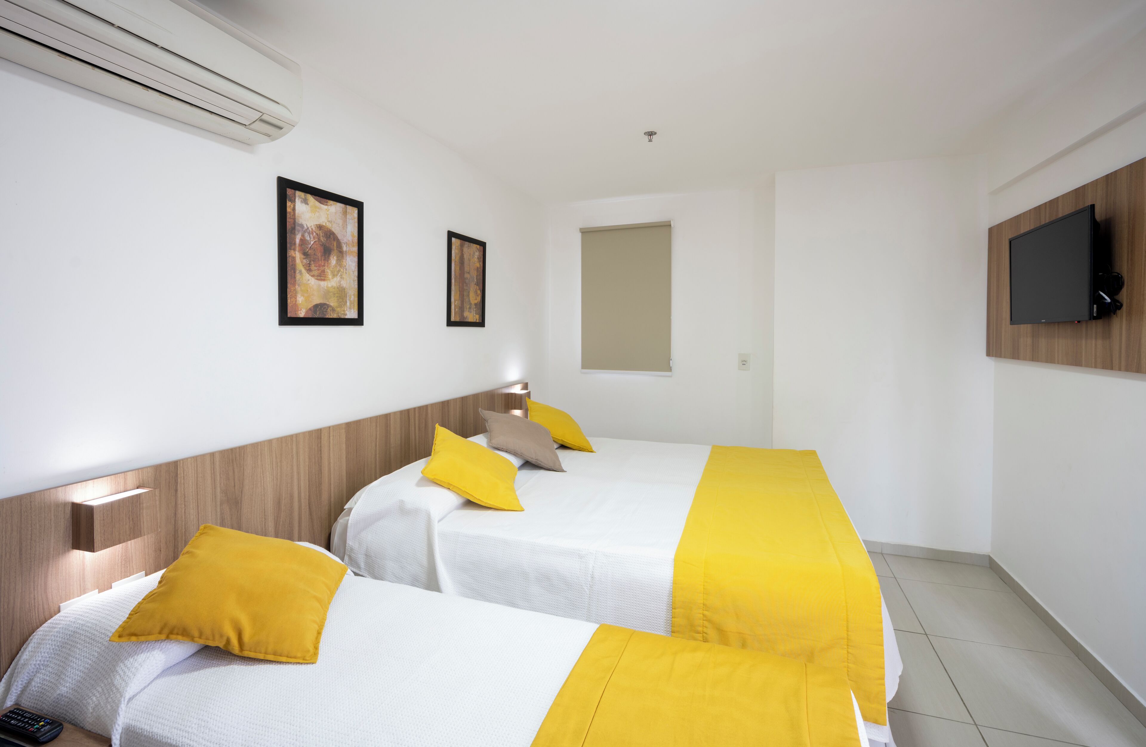 A hotel room with two beds, a mounted TV, and artwork on the walls.