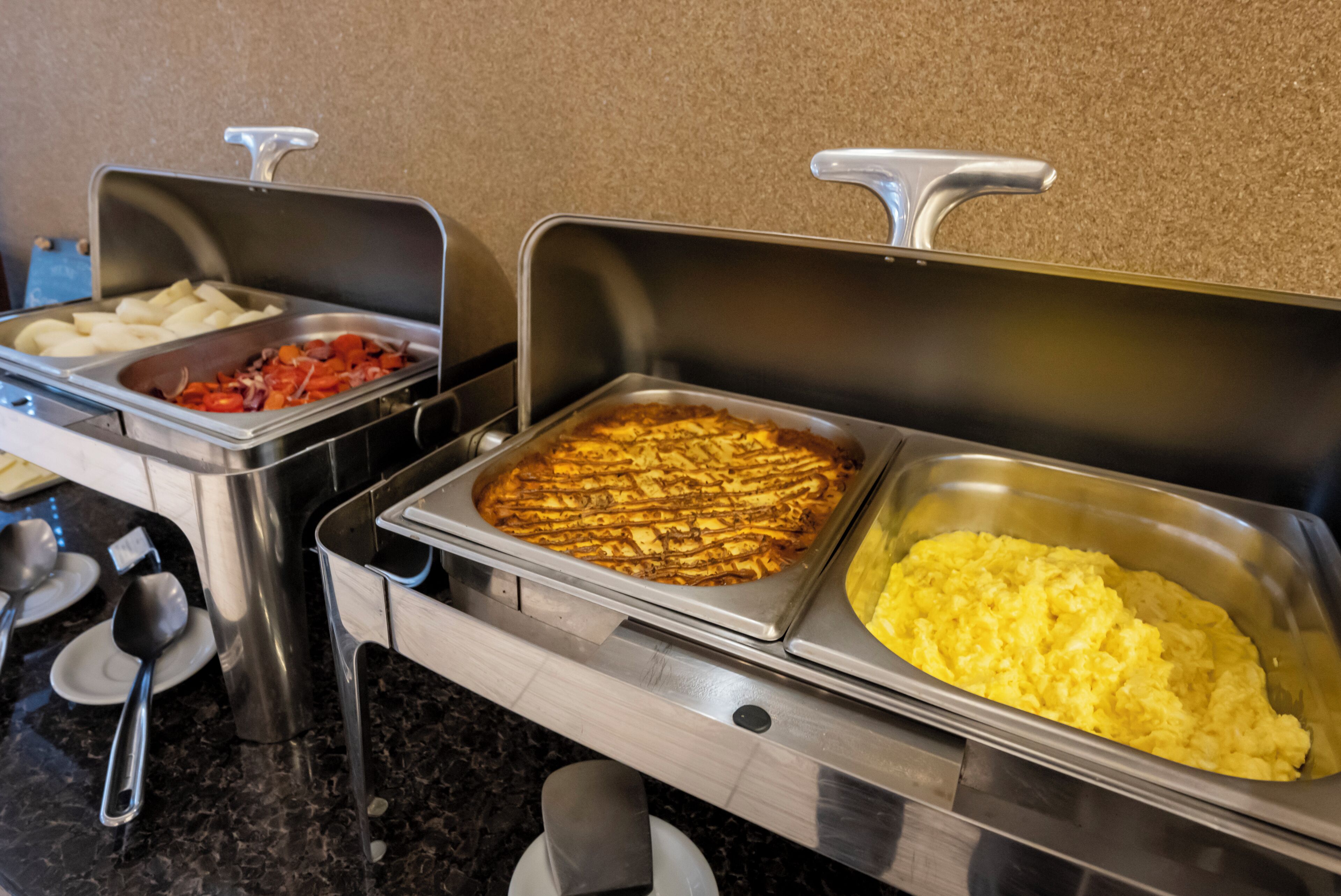 Ein Buffet mit verschiedenen Speisen, darunter Kartoffeln, gegrilltes Gemüse und Rührei.