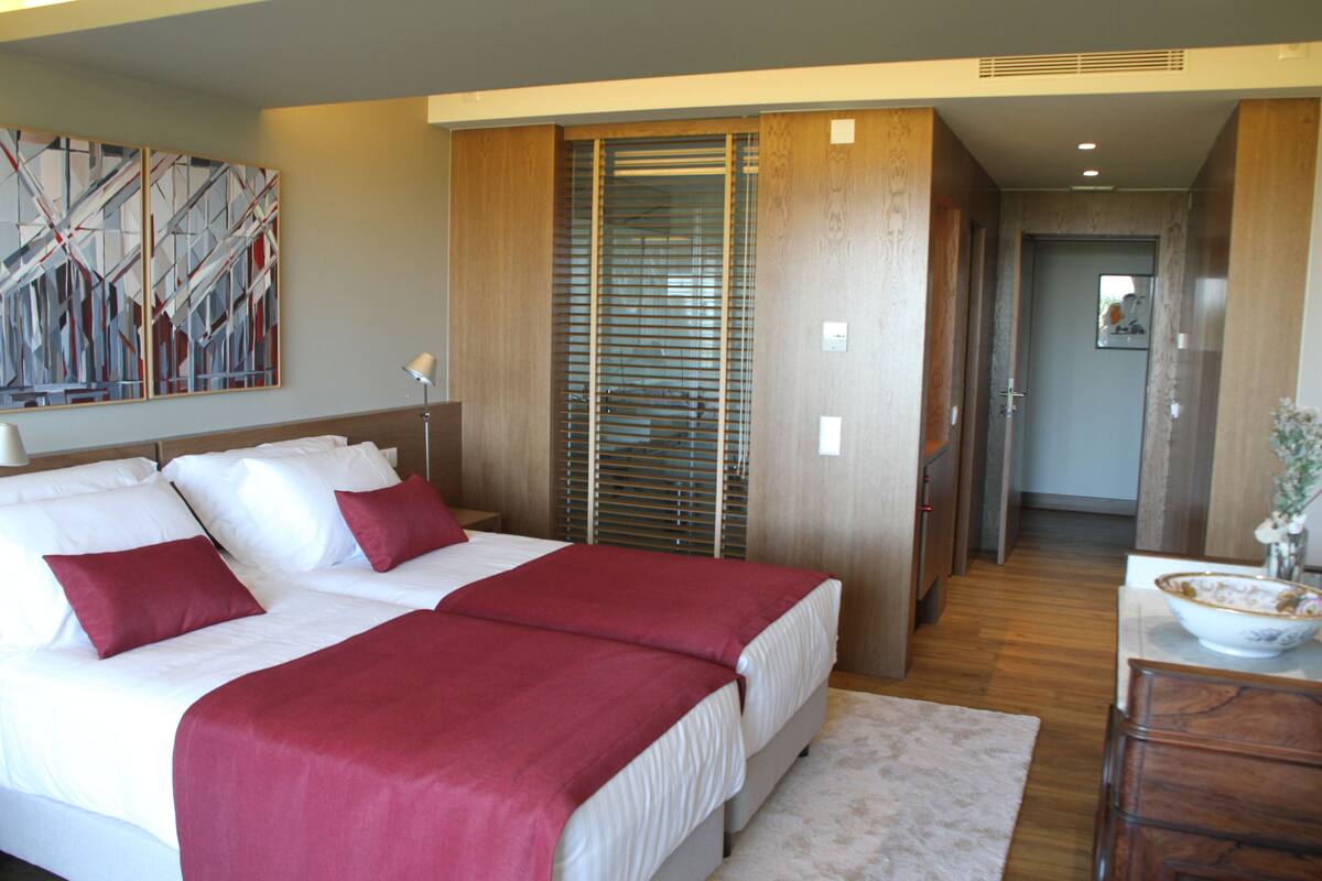 A hotel room with a large bed, a wooden wardrobe, and a painting on the wall.