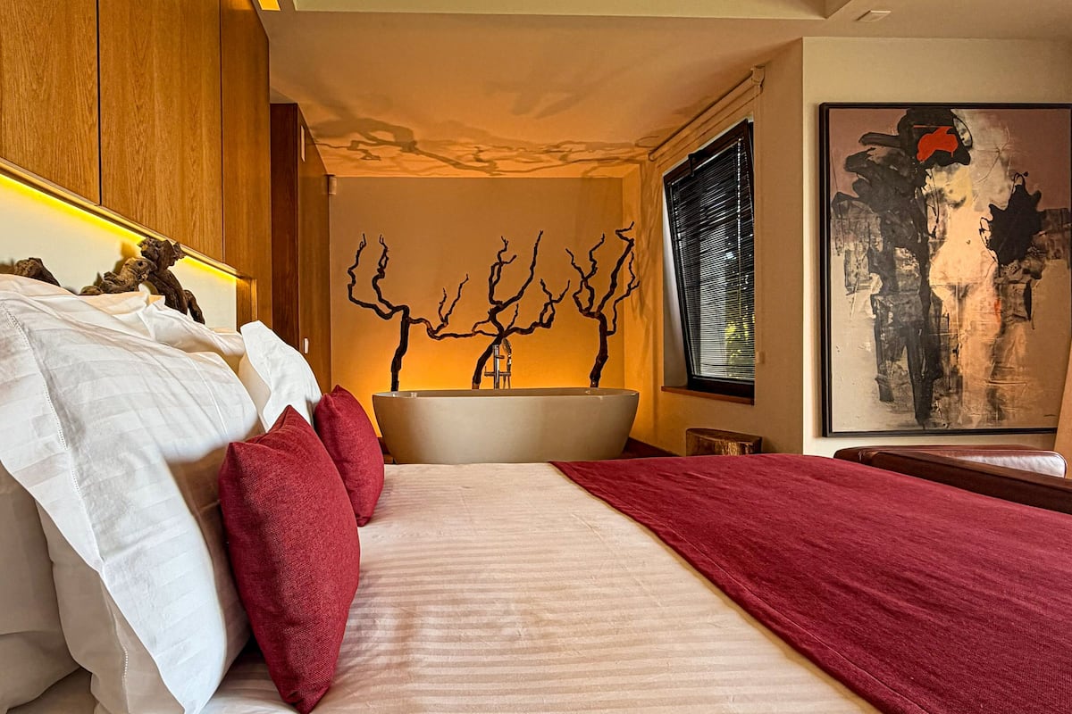 A bedroom with a large bed, a bathtub, and a wall-mounted artwork.