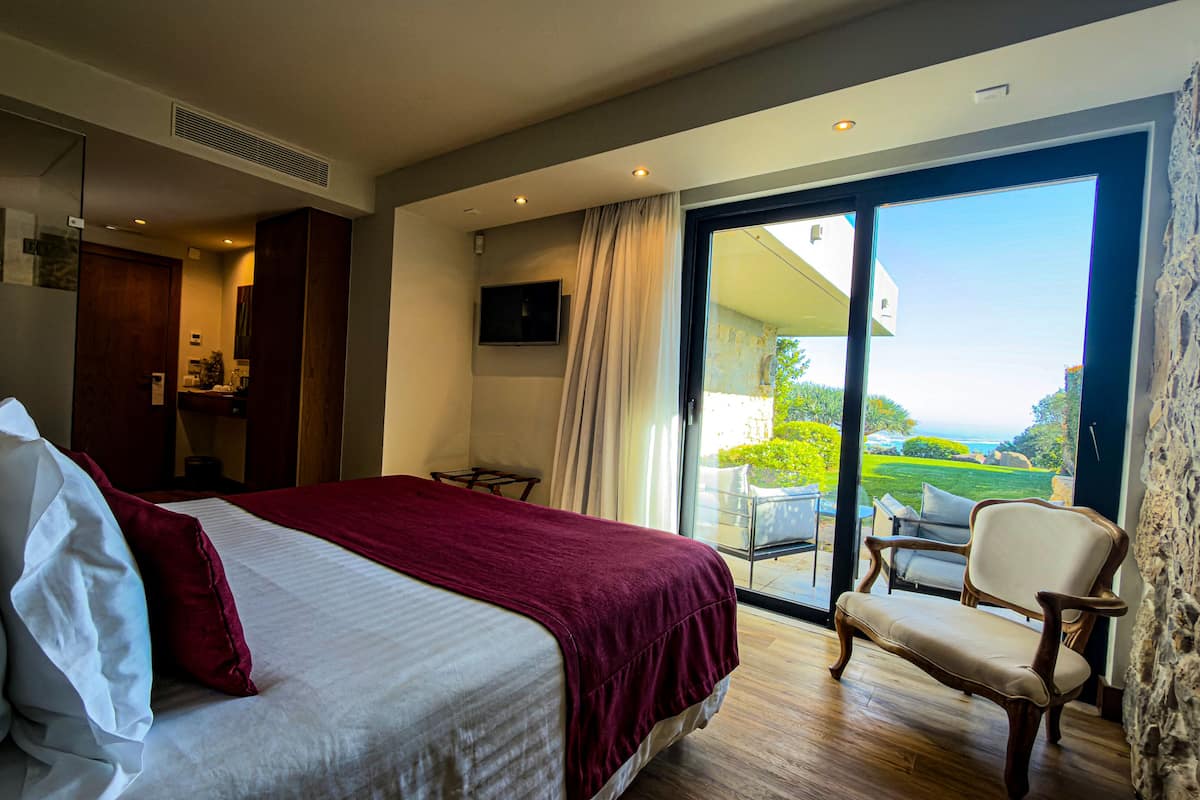 A bedroom with a large bed, a chair, a TV, and a balcony with a view.