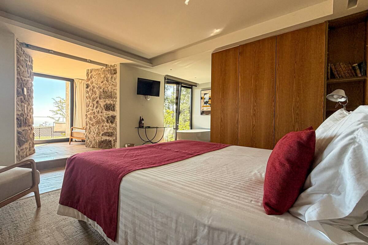 A bedroom with a bed, a chair, a TV, a wooden wardrobe, and a balcony.