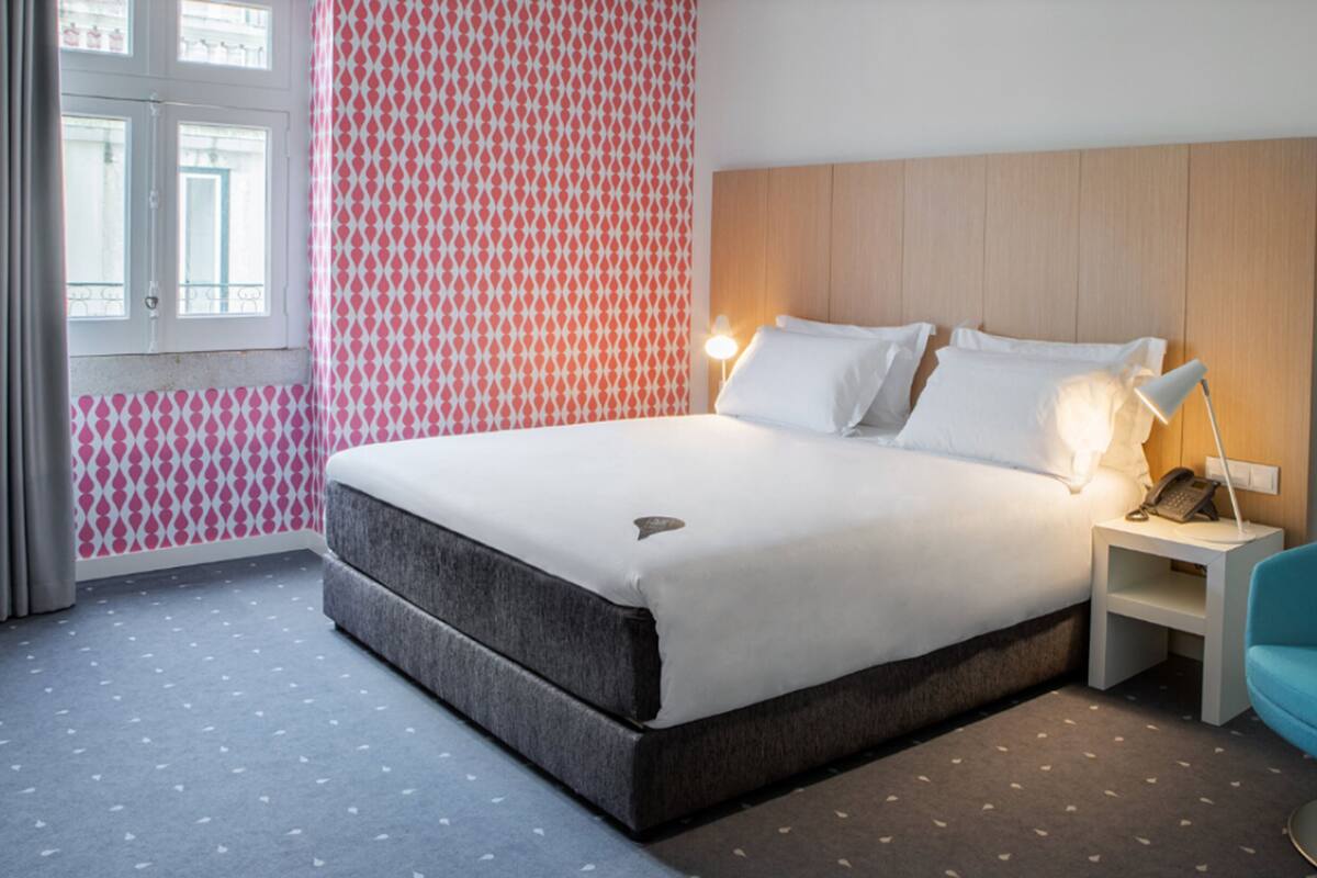 Ein Hotelzimmer mit einem Bett, einem Nachttisch, einem blauen Sessel und einer Wand mit Muster.