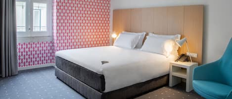 A hotel room with a bed, a nightstand, a blue chair, and a patterned wall.