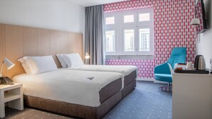 Une chambre d’hôtel comprenant un lit, une table de chevet, une lampe, une chaise et un bureau avec une bouilloire et une tasse.