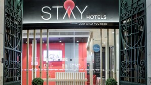 L’entrée d’un hôtel, avec une enseigne indiquant « STAY HOTELS » et un slogan : « TOUT CE DONT VOUS AVEZ BESOIN ».
