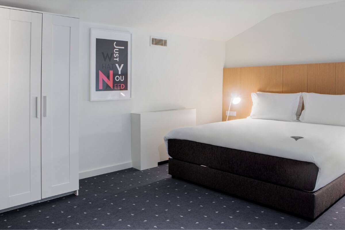 Ein Hotelzimmer mit Bett, Schrank, einem Poster an der Wand und einem Deckenventil.