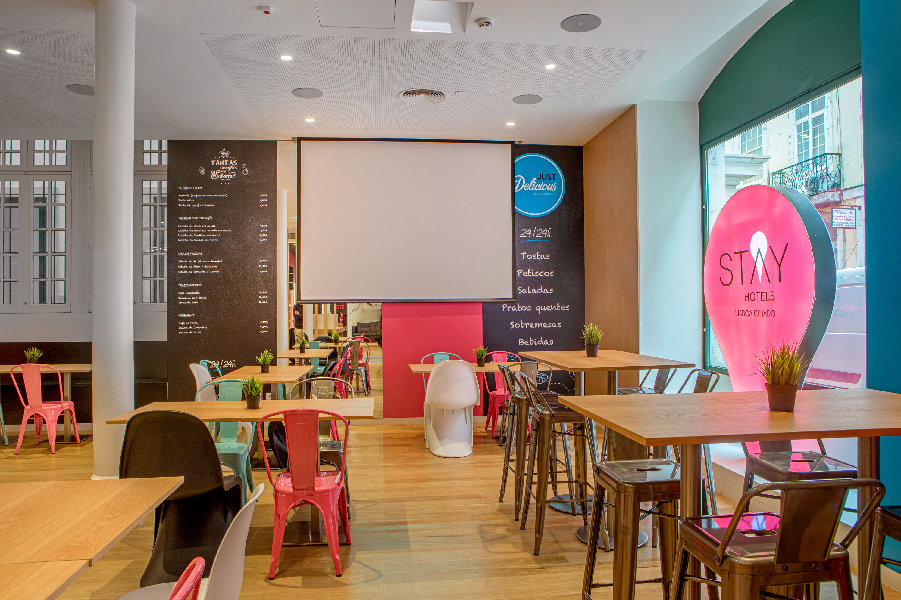 Een modern restaurant met een menubord, een groot roze bord met STAY HOTELS erop, en verschillende zithoeken.