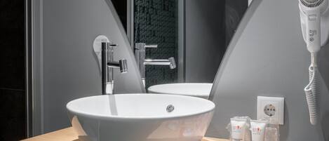 A modern bathroom with a large white sink, a mirror, a hairdryer, and toiletries on the counter.