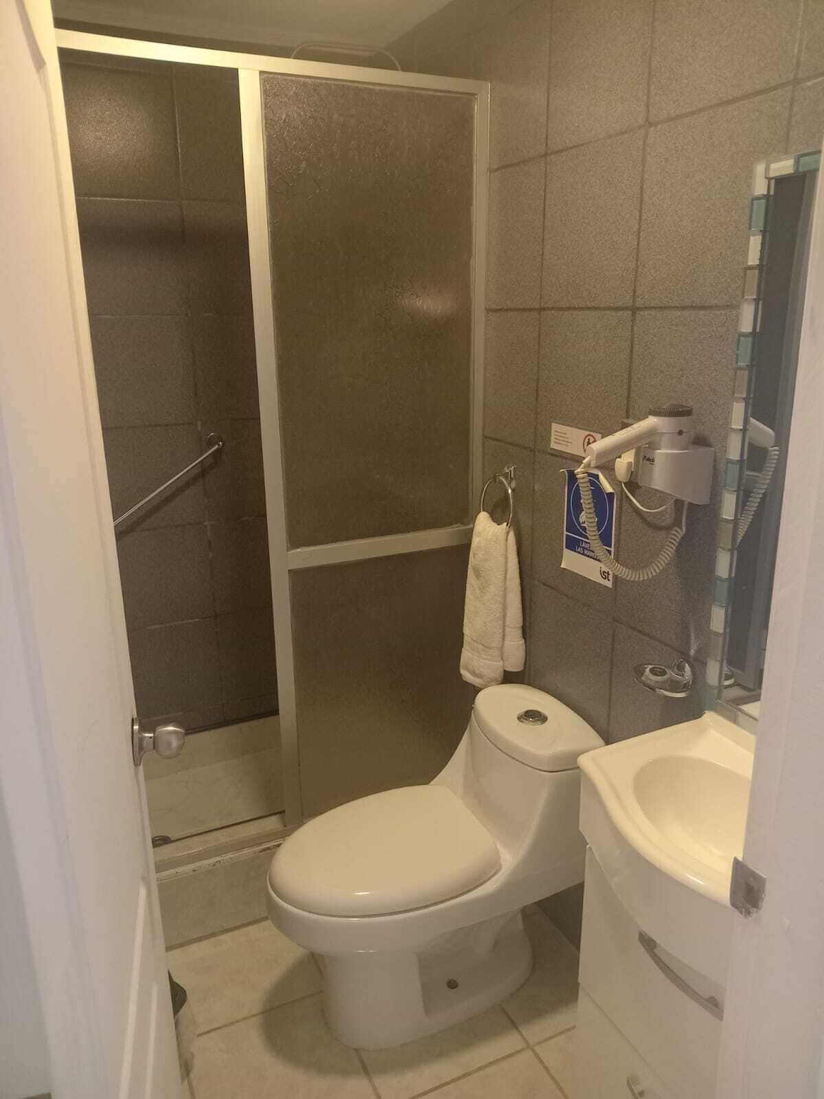 A bathroom with a shower, toilet, and a hairdryer on a wall.
