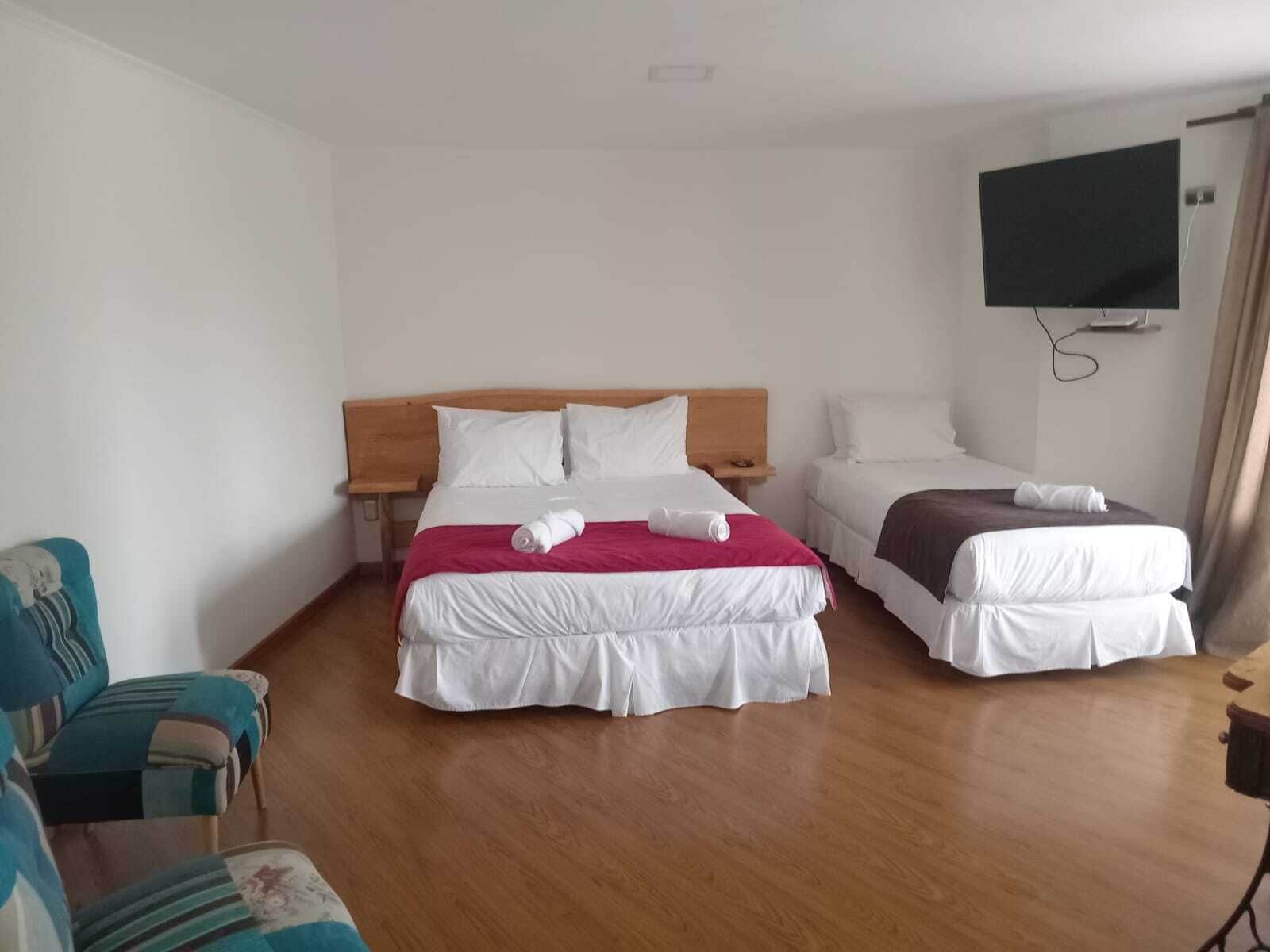 A hotel room with two beds, a TV mounted on the wall, and a wooden floor.