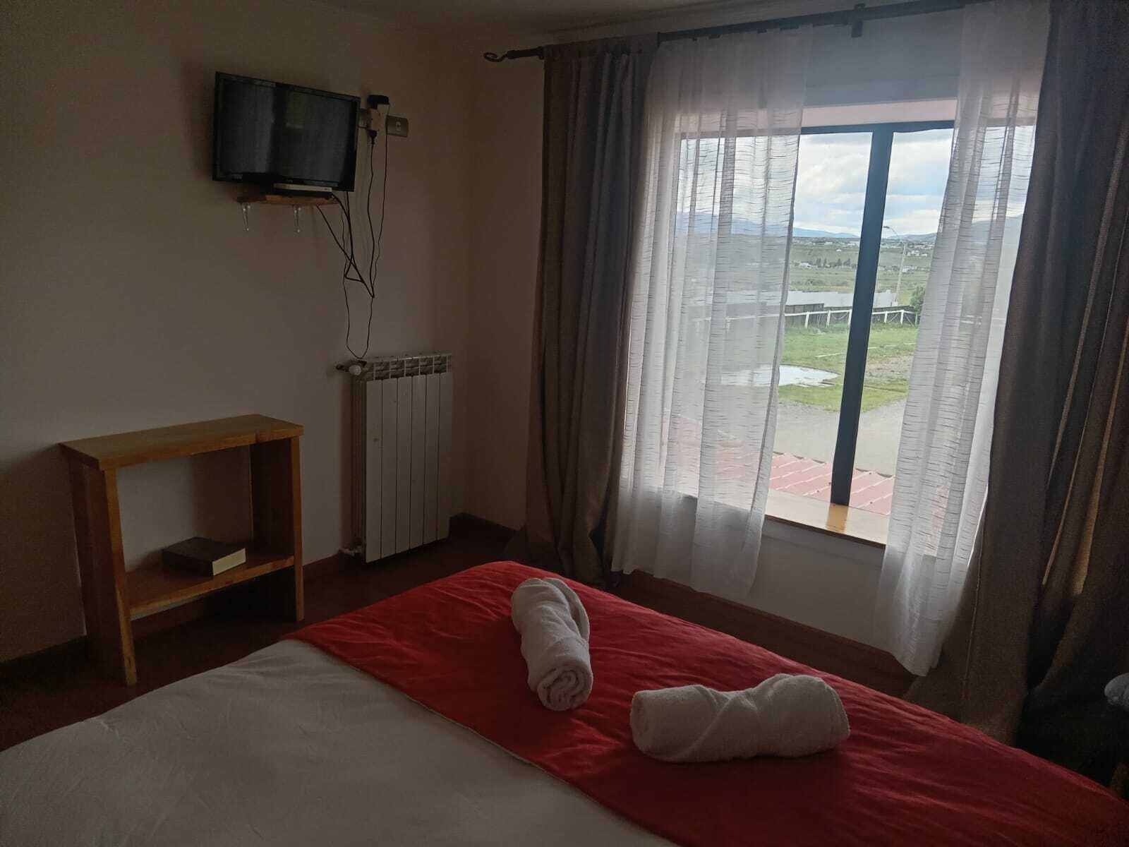 Habitación de hotel con cama, televisión montada en la pared, radiador y ventana con cortinas.