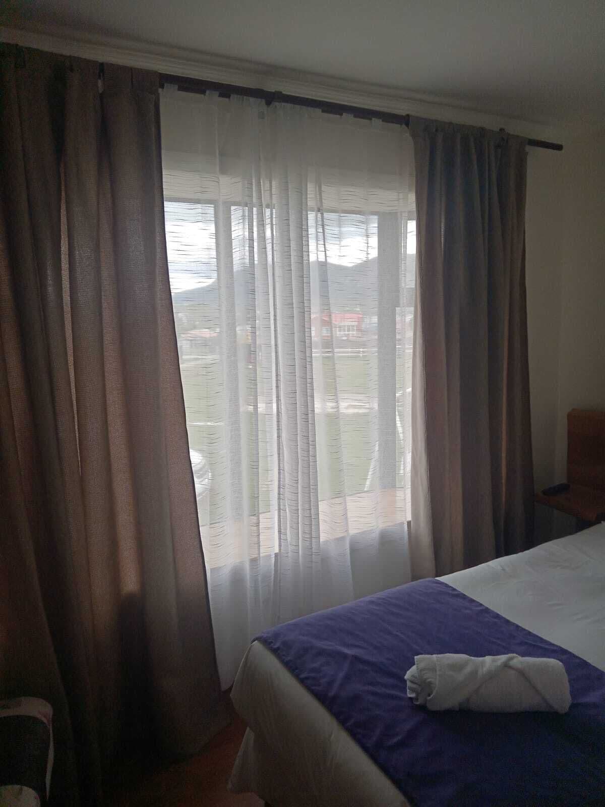 A hotel room with a bed, a chair, and a window with curtains.
