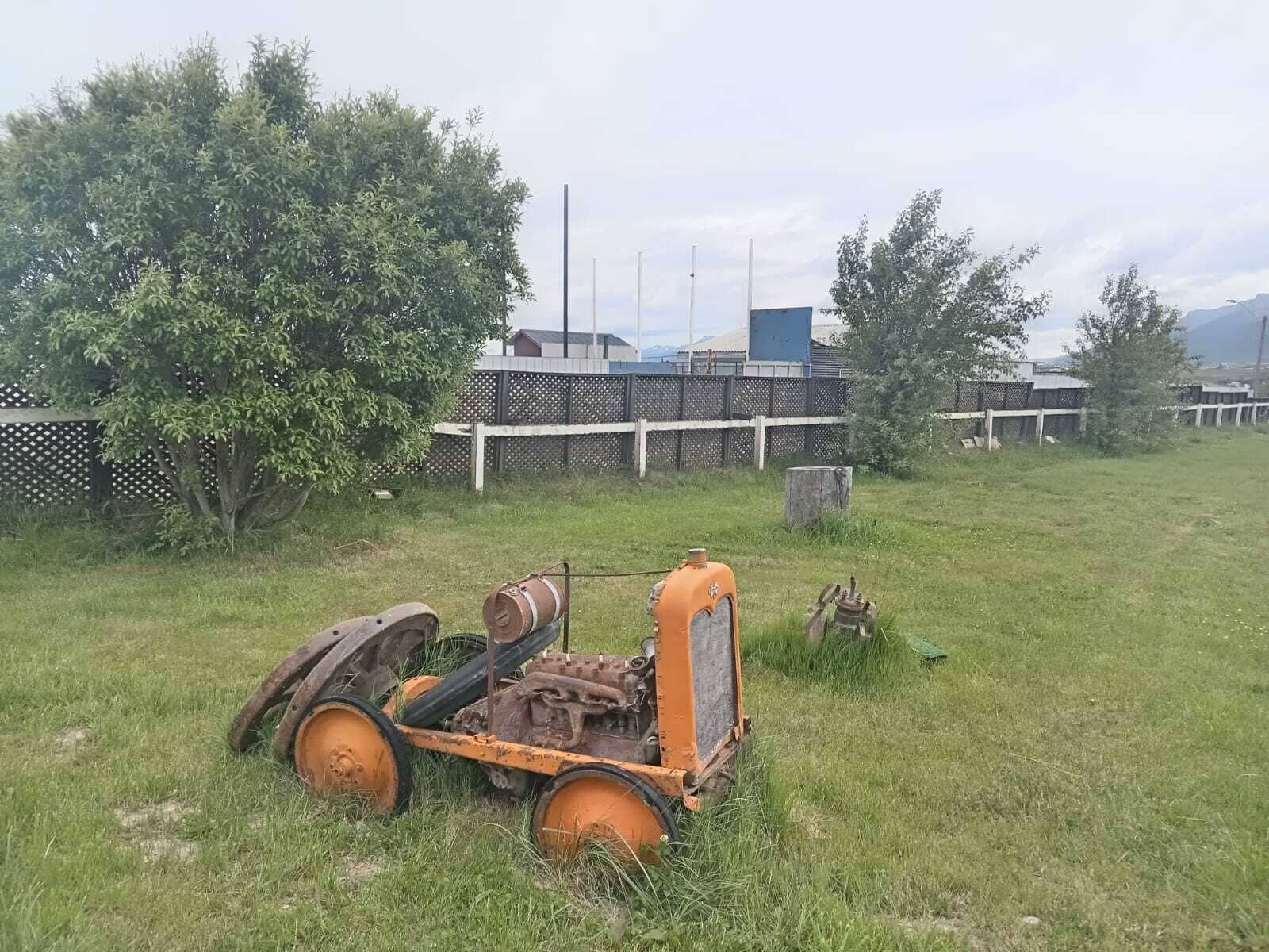 A tractor in a grassy field with trees and a fence in the background.