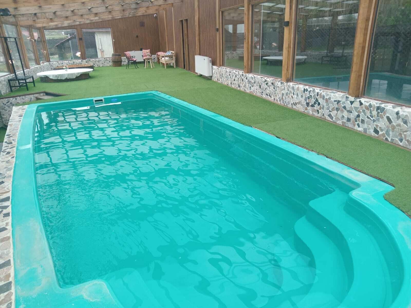 Une piscine bordée de pierres, entourée d’un mur de pierres et d’une pelouse aménagée avec du mobilier d’extérieur.