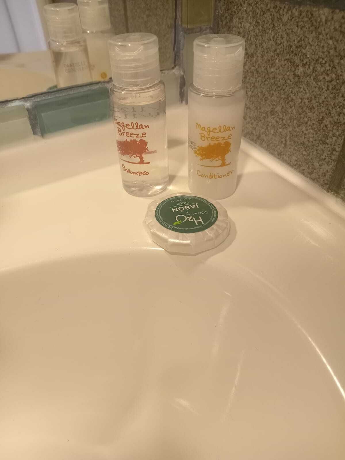 Un lavabo da bagno con due flaconi di shampoo e balsamo Magellan Breeze, e un flacone verde di shampoo idratante H2O Pure.