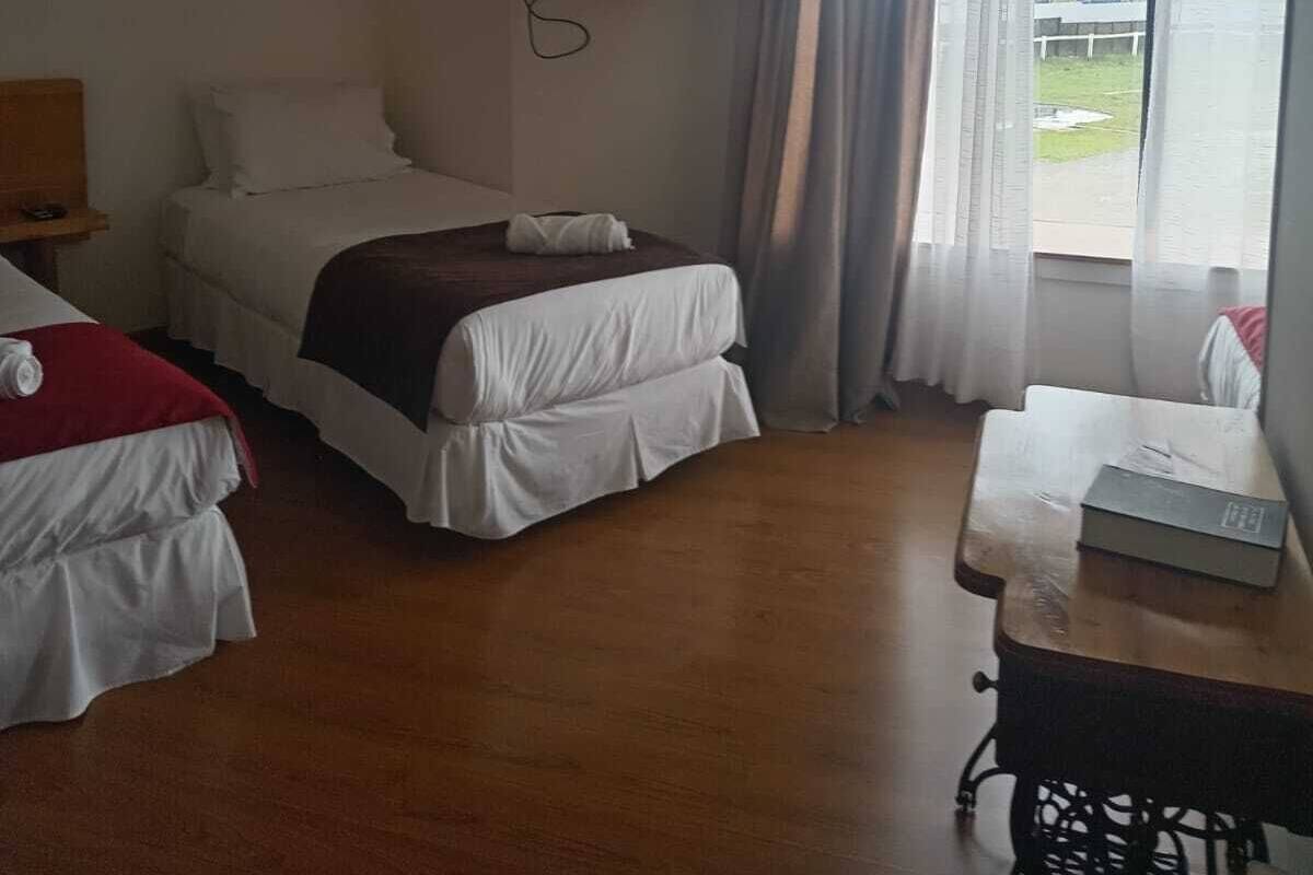 Habitación de hotel con cama, televisor montado en la pared, una mesa con una caja y una ventana con cortinas.