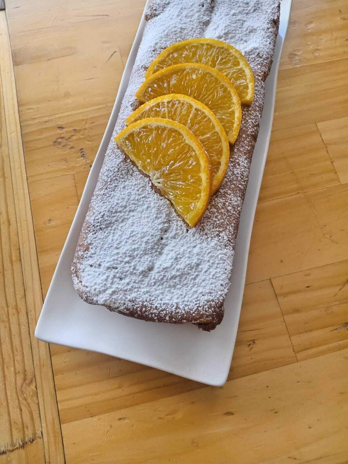 A rectangular white plate with a dessert topped with powdered sugar and orange slices.