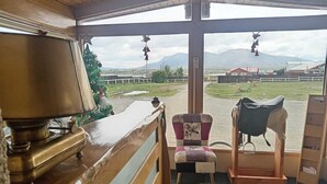 Een kamer met een houten bureau, een stoel, een zadel en uitzicht op een landelijk landschap met bergen en gebouwen.