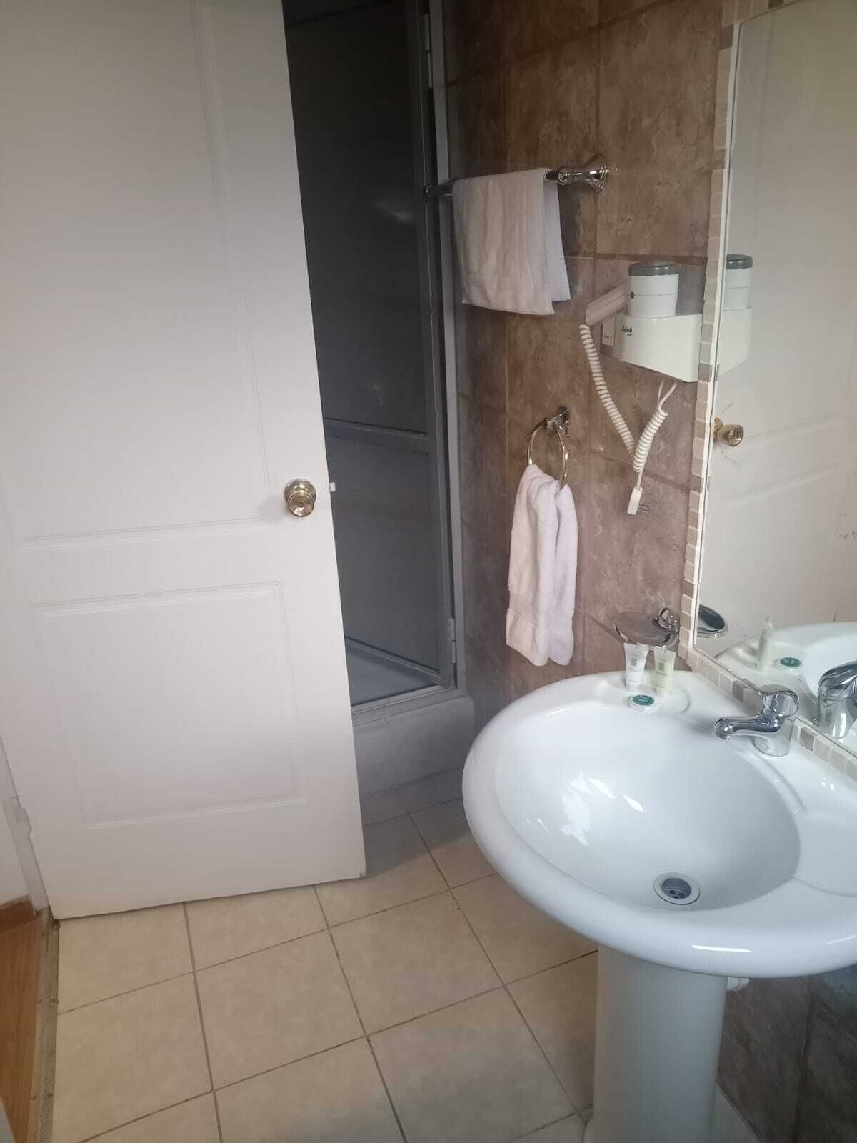 Un baño con lavamanos blanco, espejo, toallero y zona de ducha.