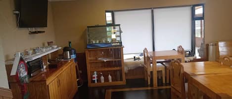 Una habitación acogedora con una mesa de madera, sillas, un acuario y un televisor en la pared.