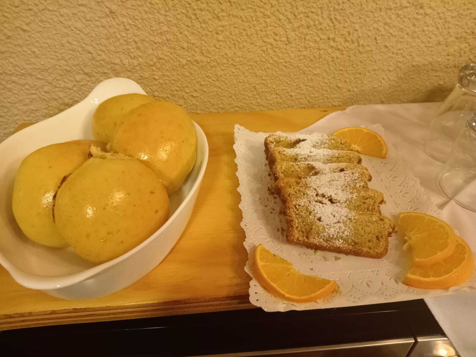 Een witte schaal met drie gele items en een sneetje brood bestrooid met poedersuiker, op een witte placemat, vergezeld van oranje partjes.