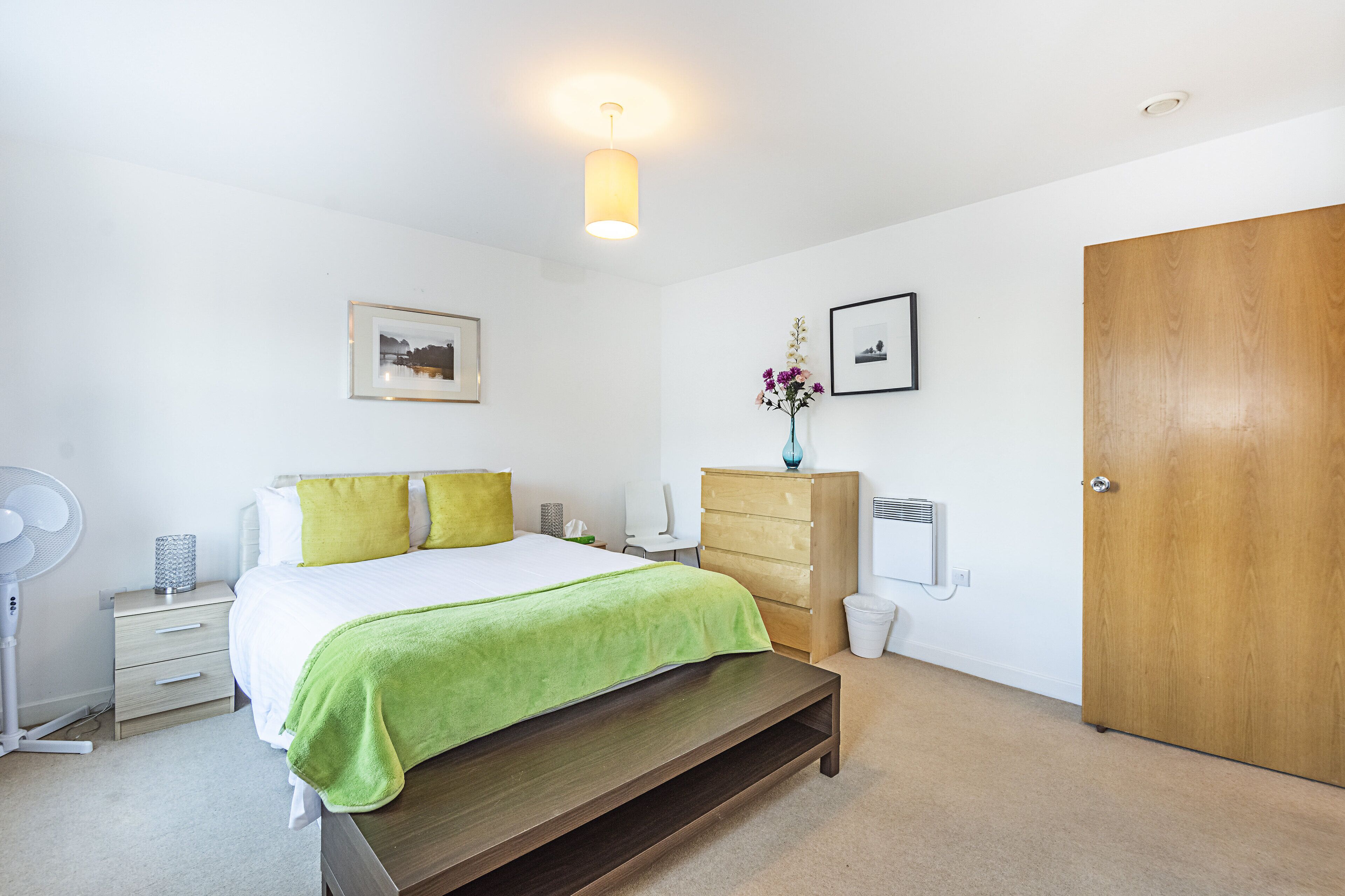 Une chambre à coucher comprenant un lit, une table de chevet, une commode et une porte en bois.