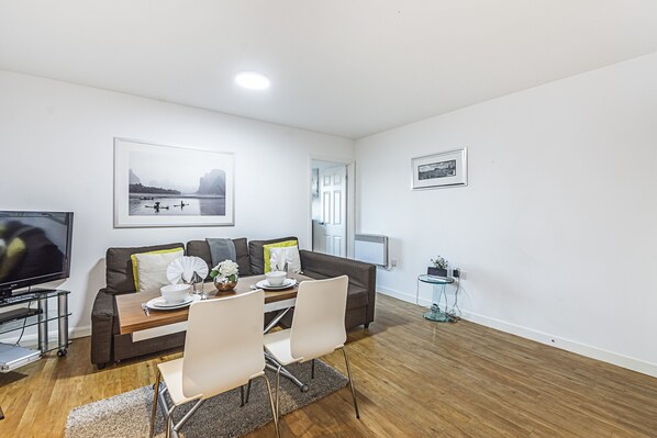 A modern living room with a sofa, dining table, chairs, a flat-screen TV, and artwork on the walls.