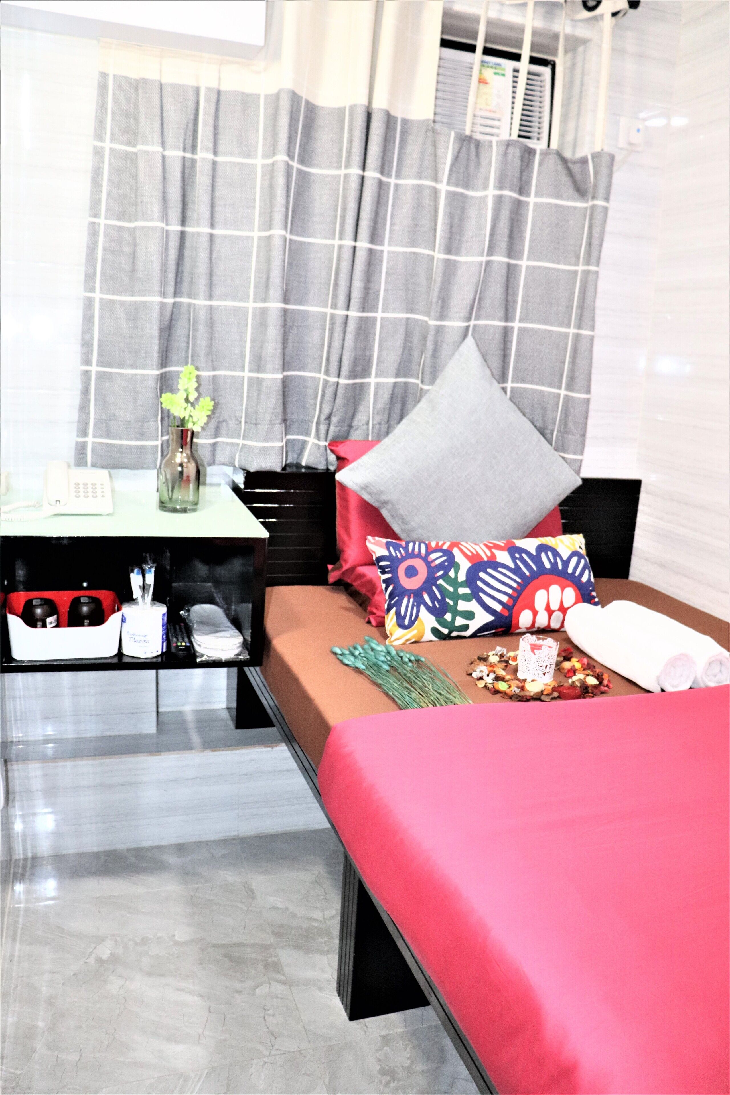 A hotel room with a bed, a bedside table, a small desk, and a window with curtains.